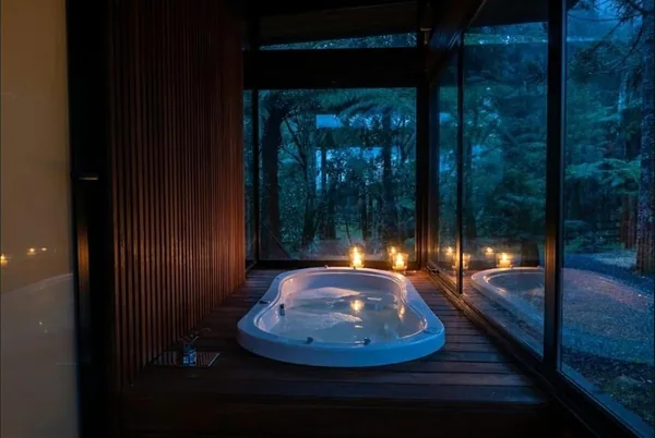 Ofurô da Cabana Cristal à noite, com velas e parede de vidro para a mata