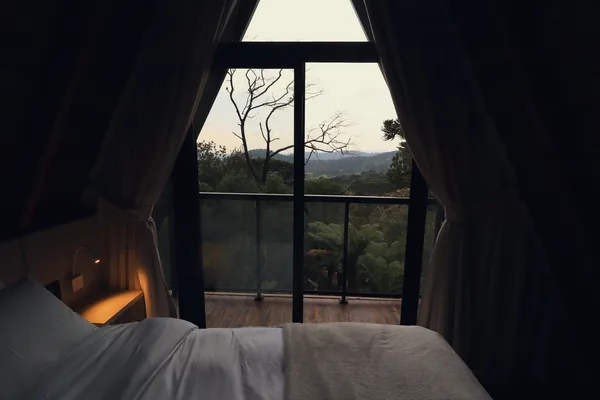 Cama da Cabana dos Pumas ao anoitecer, com a janela aberta para a mata e as montanhas
